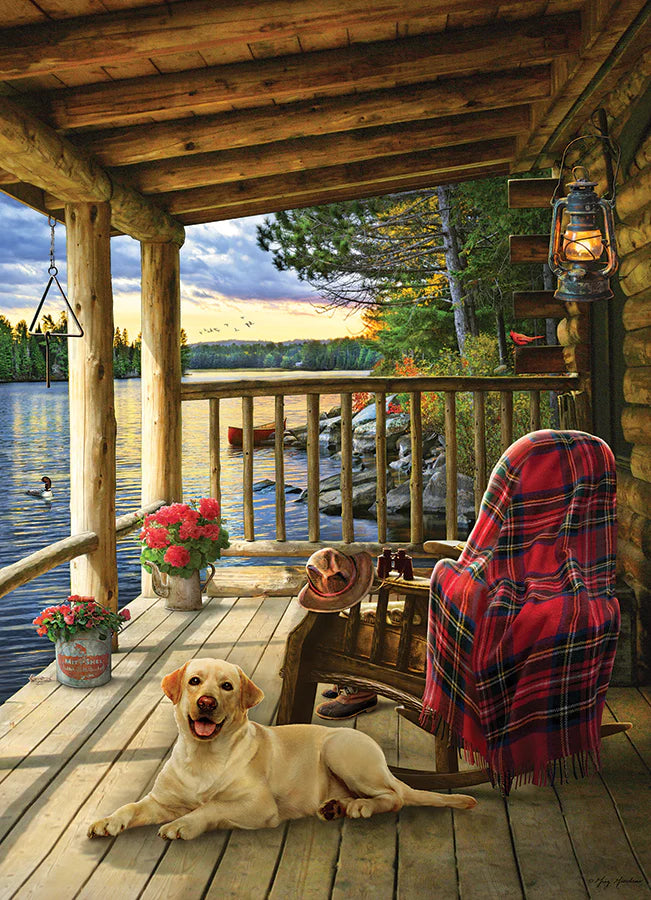 Puzzle Cobble Hill Cabin Porch – 1000 pièces. Scène paisible montrant une véranda en bois au bord d’un lac avec un chien allongé, une chaise avec couverture tartan, une lanterne suspendue, le tout sur carton rigide avec découpe aléatoire, finition lin. Illustration créée par Greg Giordano, dimensions assemblée env. 67,5 × 48,8 cm.